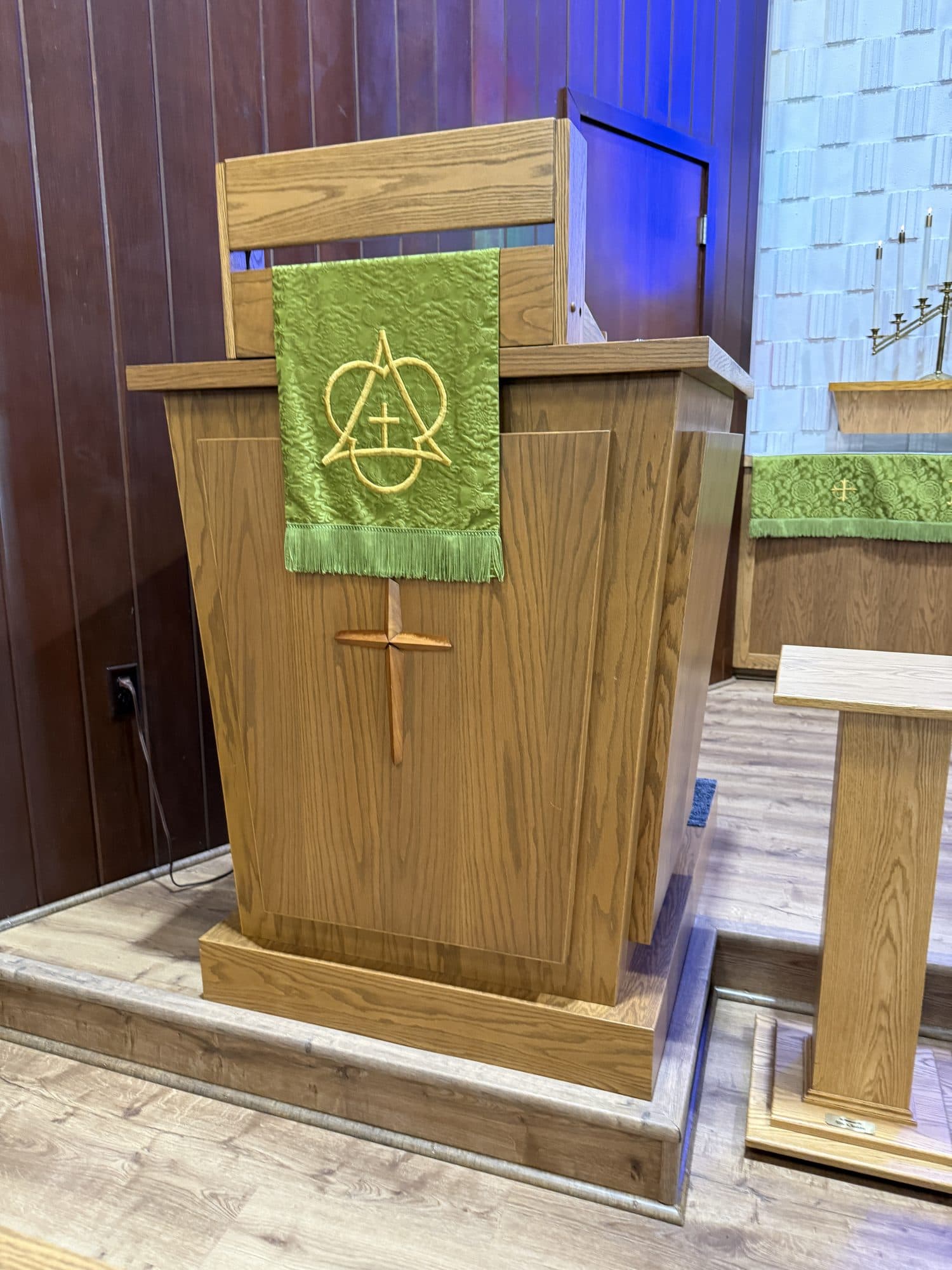 The oak pulpit with a carved cross on its front and a green fall bearing the Chi-Rho with Alpha and Omega